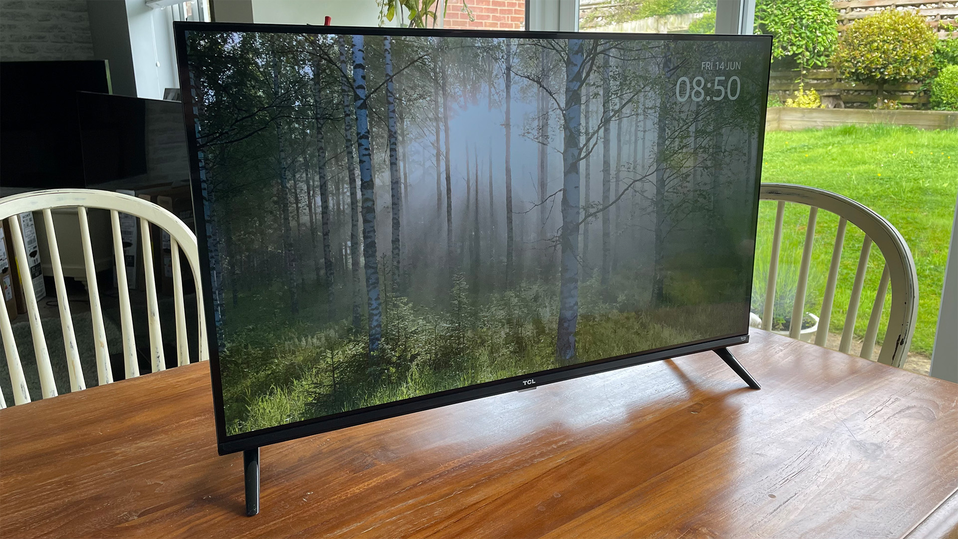 TCL 32SF540K 32英寸电视，木质餐桌，屏幕上显示树木