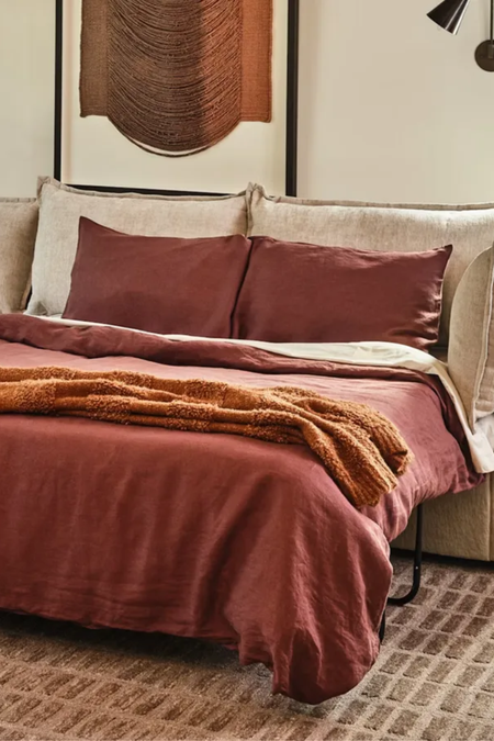 Cozy, neutral living room featuring a geometrically patterned rug and a light beige sleeper sofa styled with oxblood bed linen