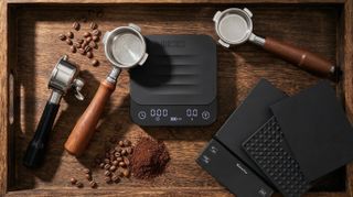an image with three portafilters, three coffee scales, on a wooden background, showing coffee beans and ground coffee