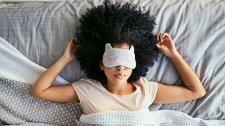 A woman wearing a sleep mask lies in bed