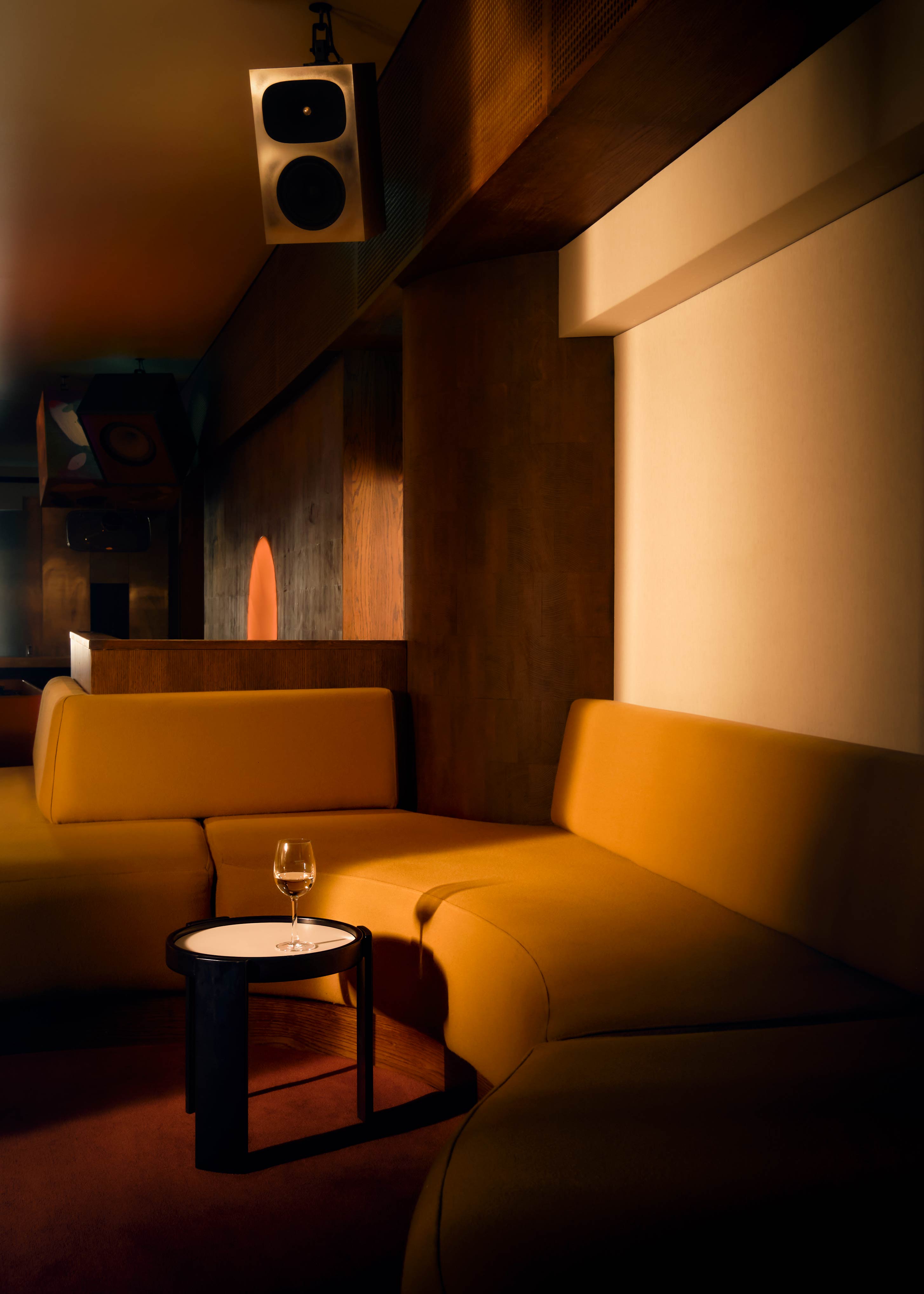 The atmospherically lit nooks of a listening bar, featuring spherical, orange-tinted light installations, wood and chrome surfaces, and plush, earthy textiles.