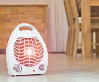 A little white space heater warming a dining room, with blurred wooden tables and chairs in the background.