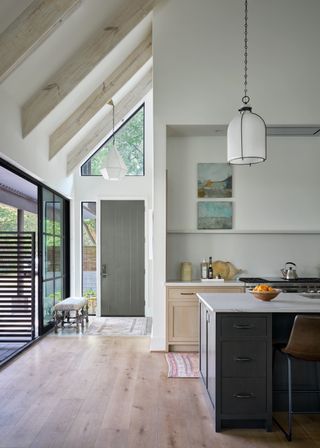 A kitchen extension with wood flooring and an island in the middle. Above the island is a light pendant.