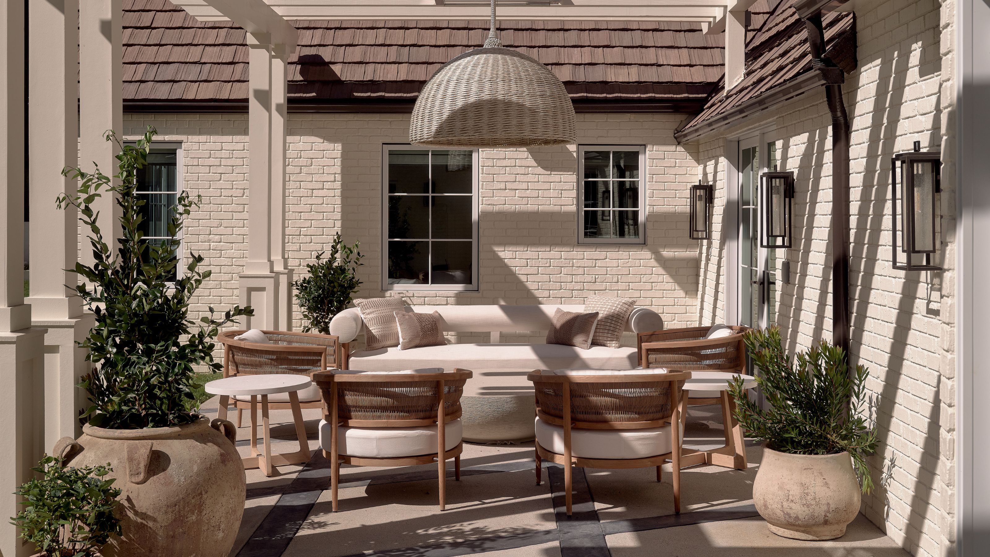 a covered tucked away patio with white painted brick walls and a wicker and neutral set of furniture