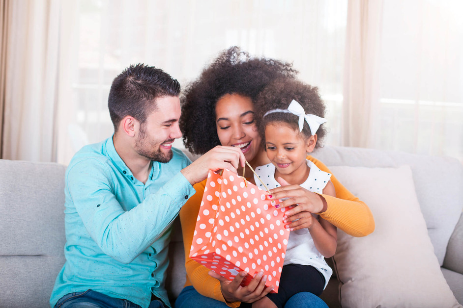 A father and mother are sitting together with their child, opening a gift. 