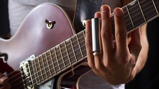 A close-up of a guitarist playing electric guitar, with a metal slide on the ring finger of his fretting hand
