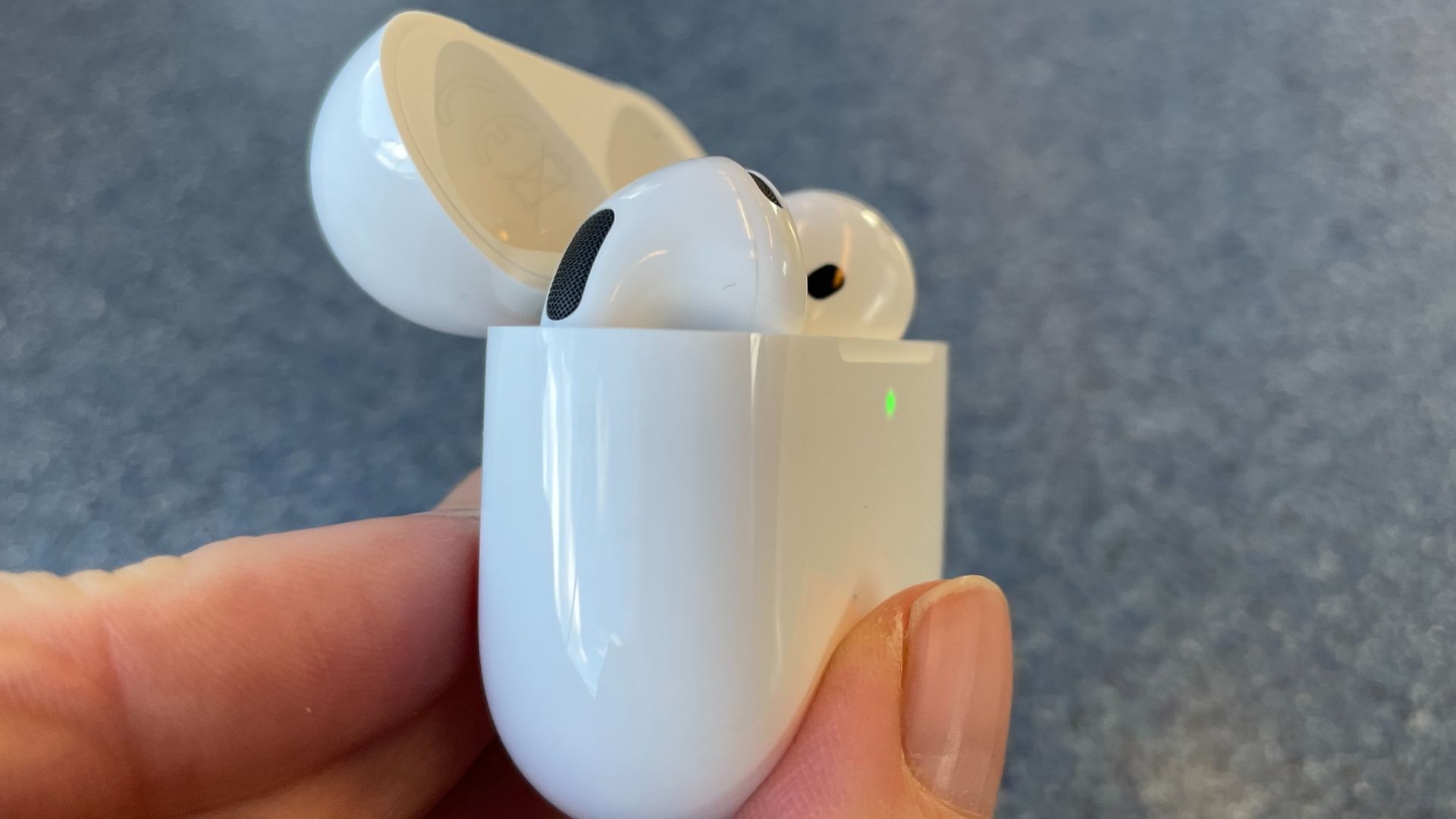 Apple AirPods 5 with Wireless Charging, on a blue table and held in a hand