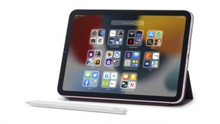 The Apple iPad Mini (2020) in landscape propped up with a stand, with an Apple Pencil lying in front of it