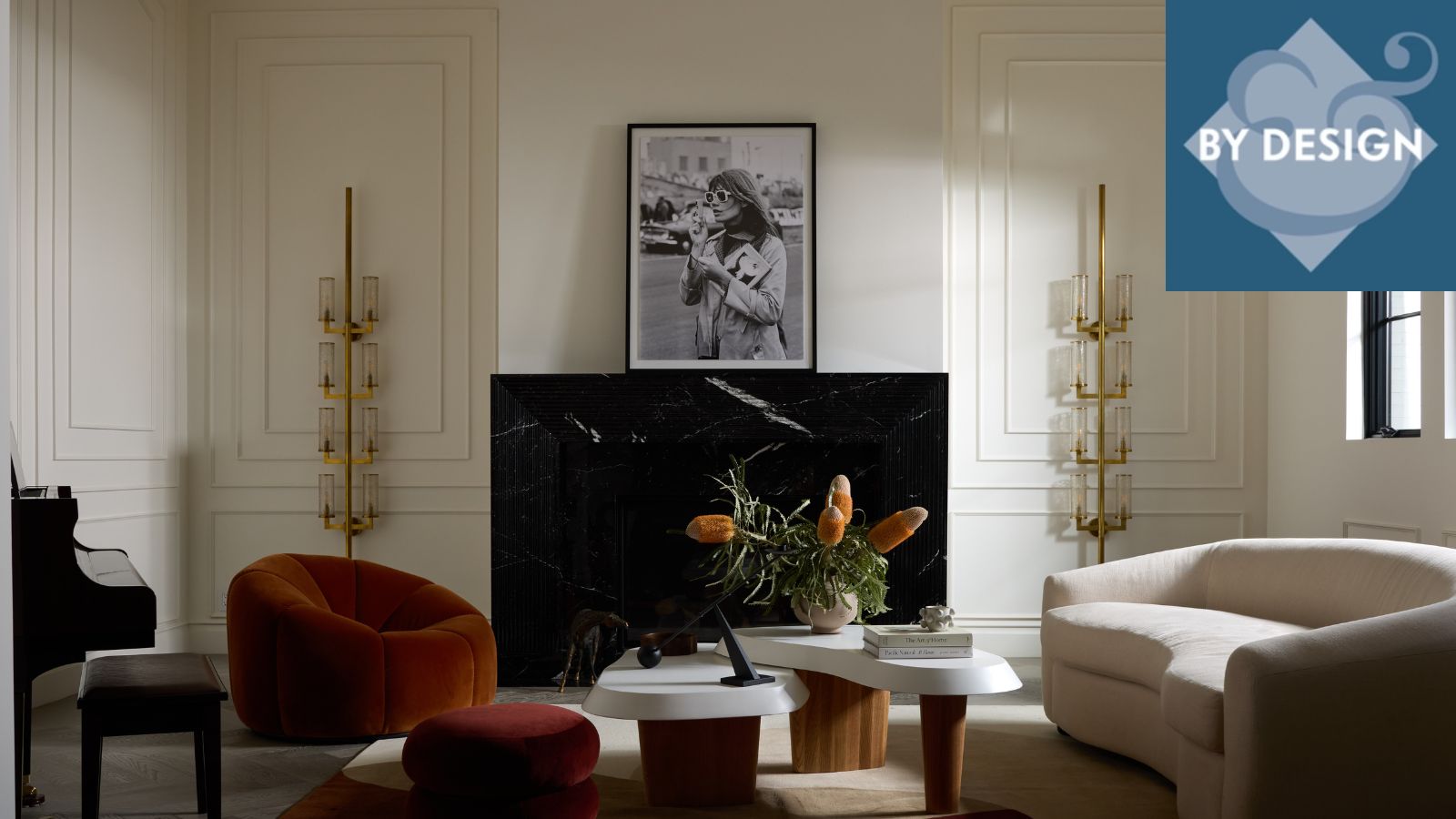 Close up of furniture in front of a black marble fireplace, mantel decorated with artwork, sculptural metallic wall light to the left hand side, geometric rug underneath furniture