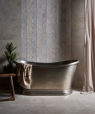 Striped tile wall with grey and blue, marble bathroom floor and large metal bathtub