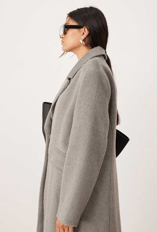 One of the best jacket coat brands, ASOS, is shown in an image of a model wearing a gray coat with a black clutch bag