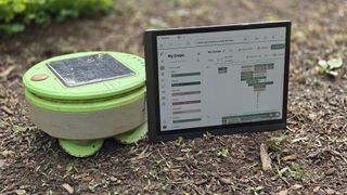 A Tertill gardening robot next to a BigMe B1051C tablet with the Seedtime app running on it