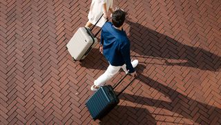A birds-eye view of two people walking each with a suitcase, one black and one white.