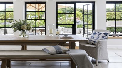 black rimmed glass doors, wooden dining table and bench and white wicker chair