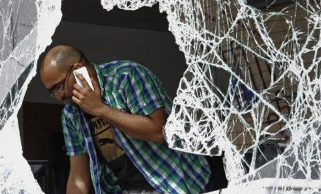 A London talks on his iPhone while assessing the damage to his looted shop: Twitter and other social media have aided the city during the cleanup. 