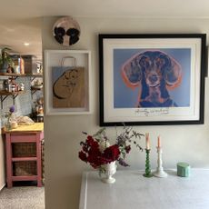Artwork of a daschund framed in a black frame on a wall neutral wall with a table in front of it and a glimpse of a kitchen behind