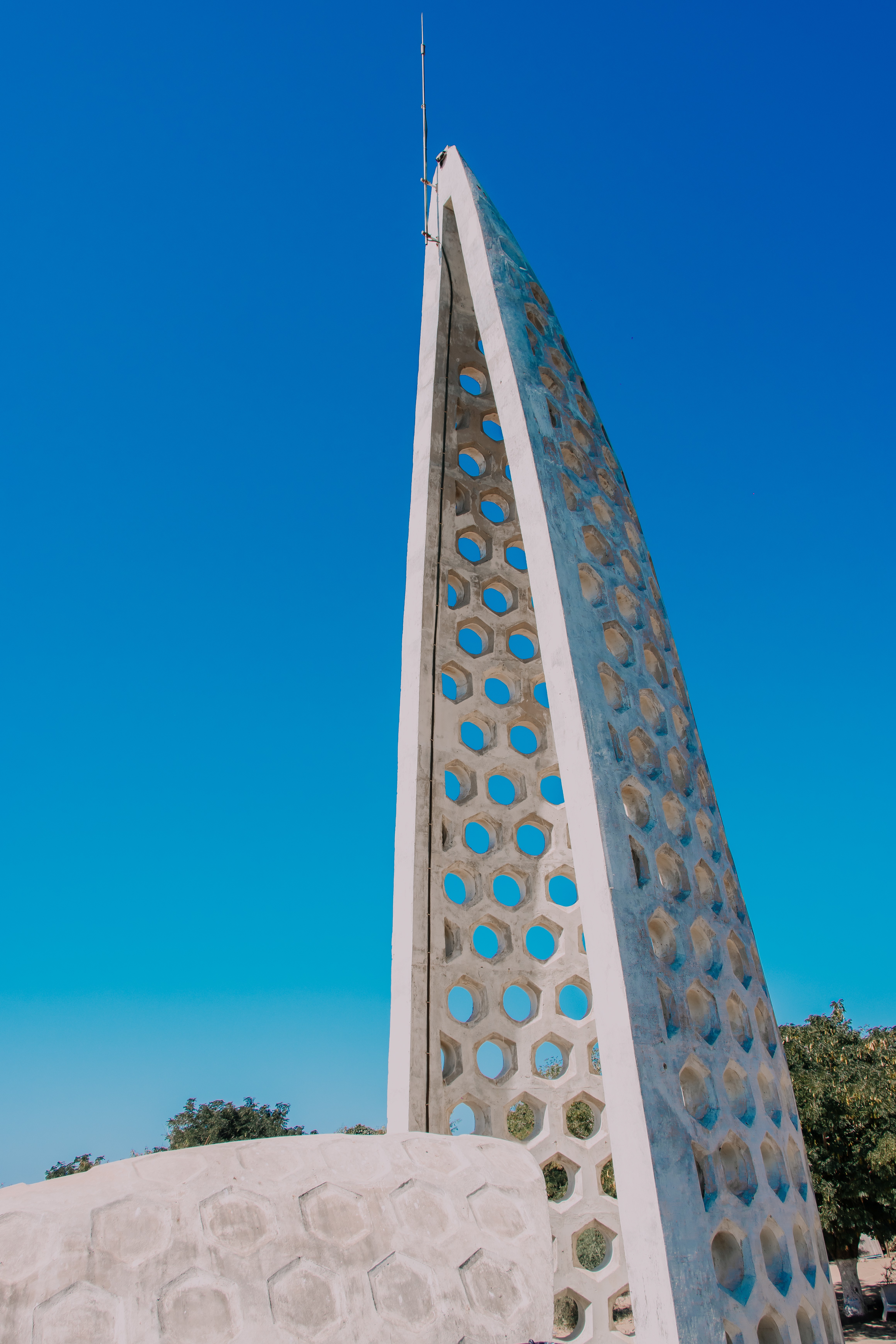 A perforated chapel wall made of concrete against a cloud-less blue sky.