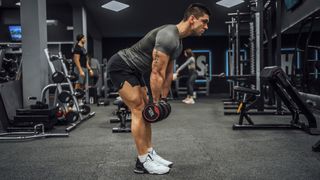 Man doing deadlift with dumbbells in a dark gym setting