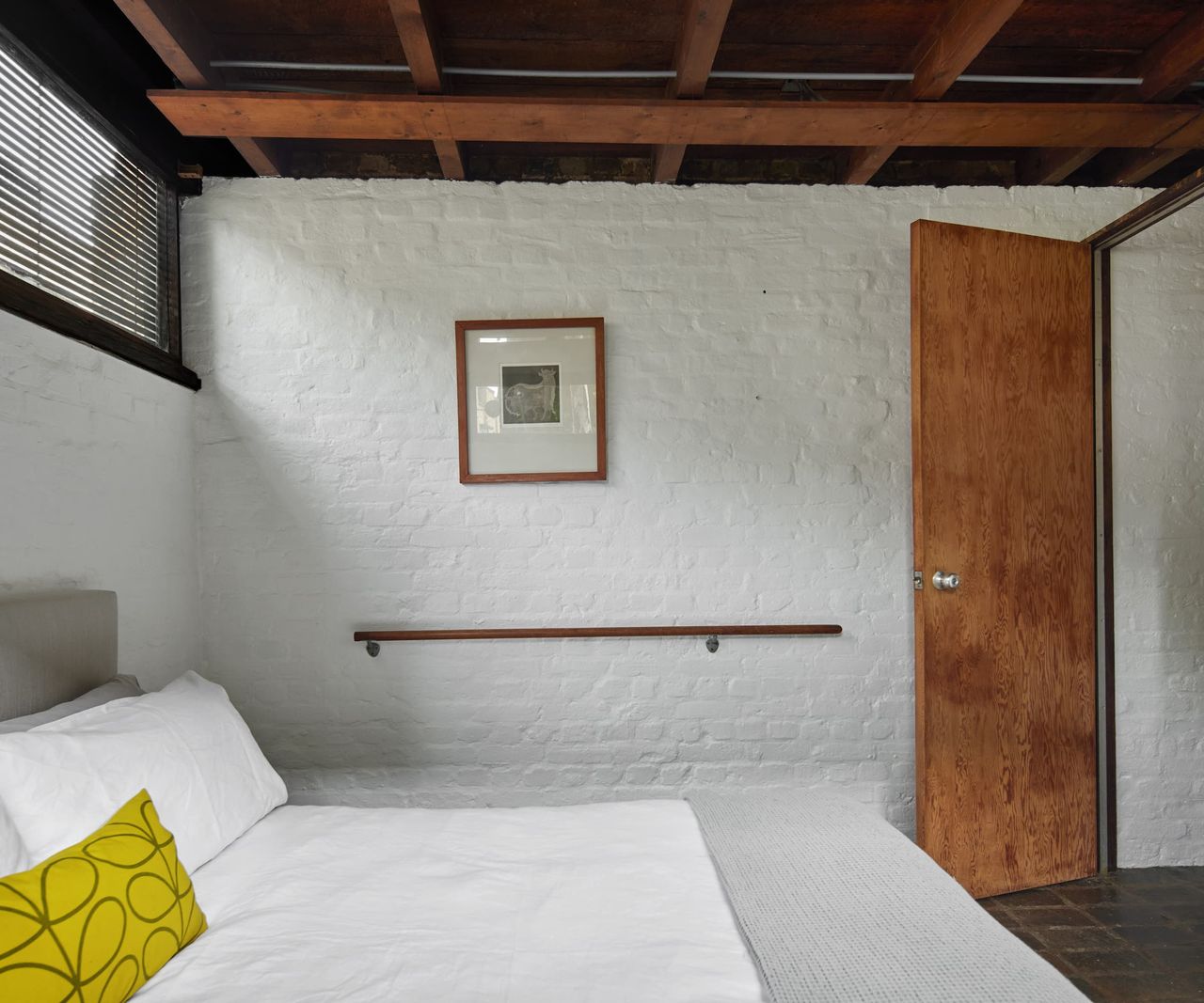 A bedroom with a handrail along the wall and wooden beamed ceiling
