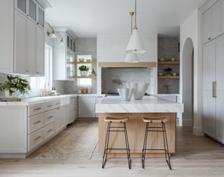 kitchen with pale gray units and white conical pendant lights with island and wooden stools and marble worktops