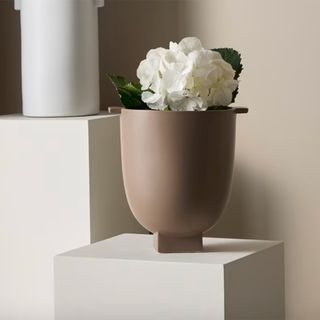 Clay urn vase on a plinth with a white hydrangea in it