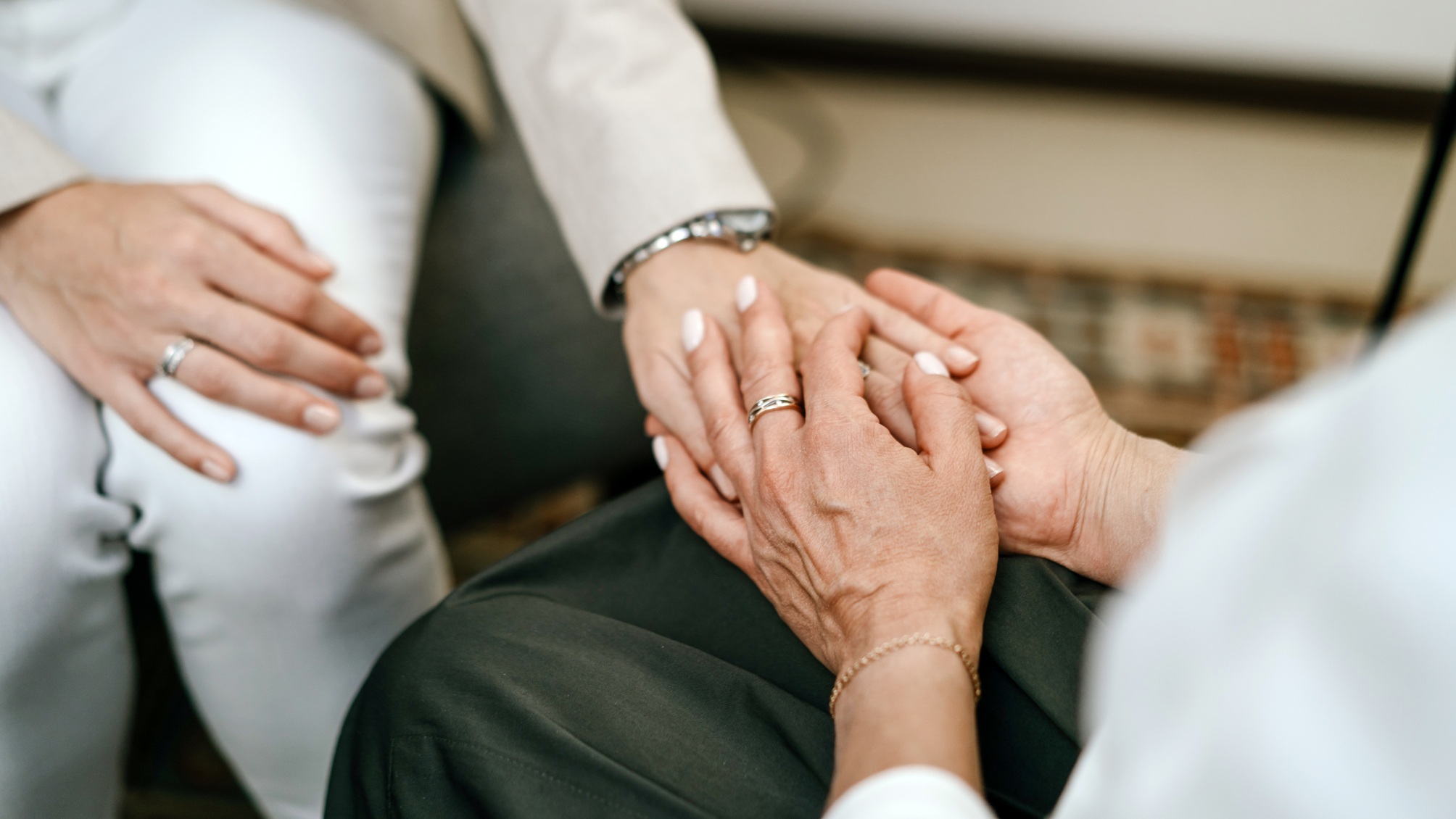 An older woman and a younger woman clasp hands as if at a memorial service, only their hands showing.