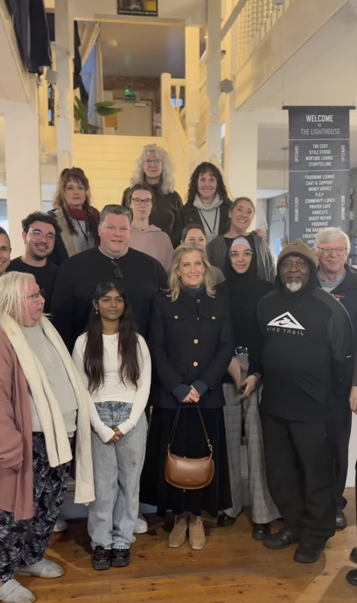 Duchess Sophie holding a tan bag, posing with a group of people in front of a staircase