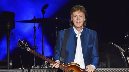 paul mccartney holding a guitar on a blue background