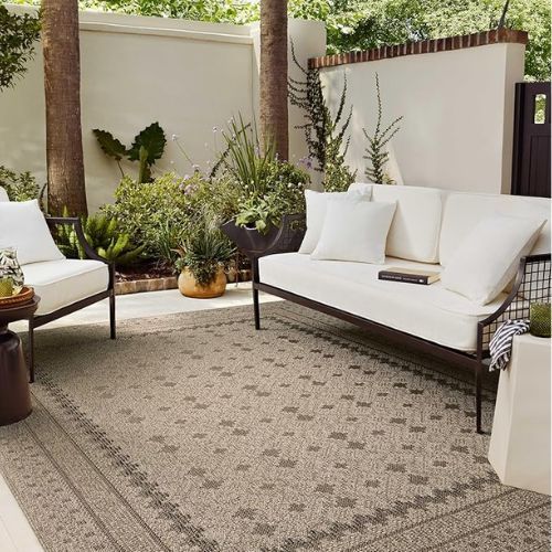 Outdoor patio with outdoor rug, black and white sofa and armchair, plantered in background