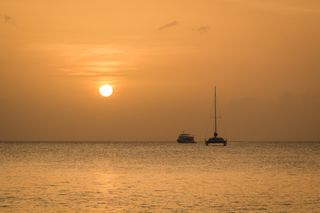 A beautiful orange sunset on Seven Mile Beach in Grand Cayman with boats on the horizon.