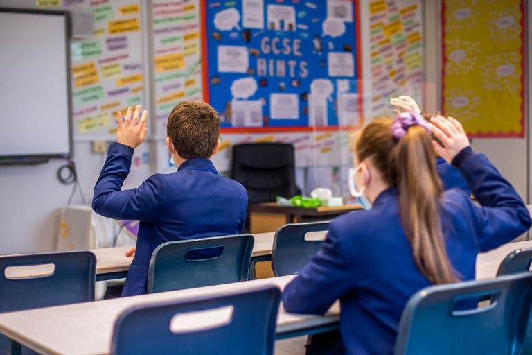 Children at school after lockdown ends, in the classroom with face masks on and hands raised