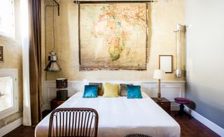 Bedroom in neutral tones and highlights of blue. An old map hangs above the bed