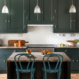 A green painted kitchen with white metro tiles and green painted bar stools in front of a marble kitchen island