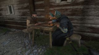 Kingdom Come Deliverance 2 money: Two people sat at a table playing a dice game next to a wooden building.