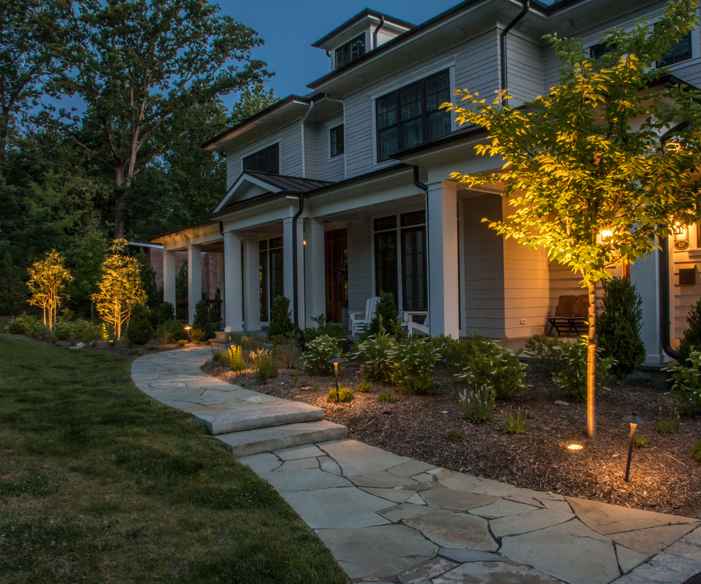 front garden design with curved pathway, lawn, flowerbeds, uplighters directed at small clipped trees, porch and house