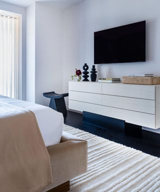 A bedroom with a white textured rug, a console table and a TV mounted to a white wall