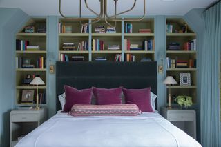 Double bed with white bedlinen, upholstered headboard in blue, two side tables and built-in bookshelves behind bed