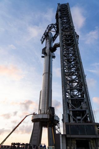 a large, shiny silver rocket sits on a launch pad