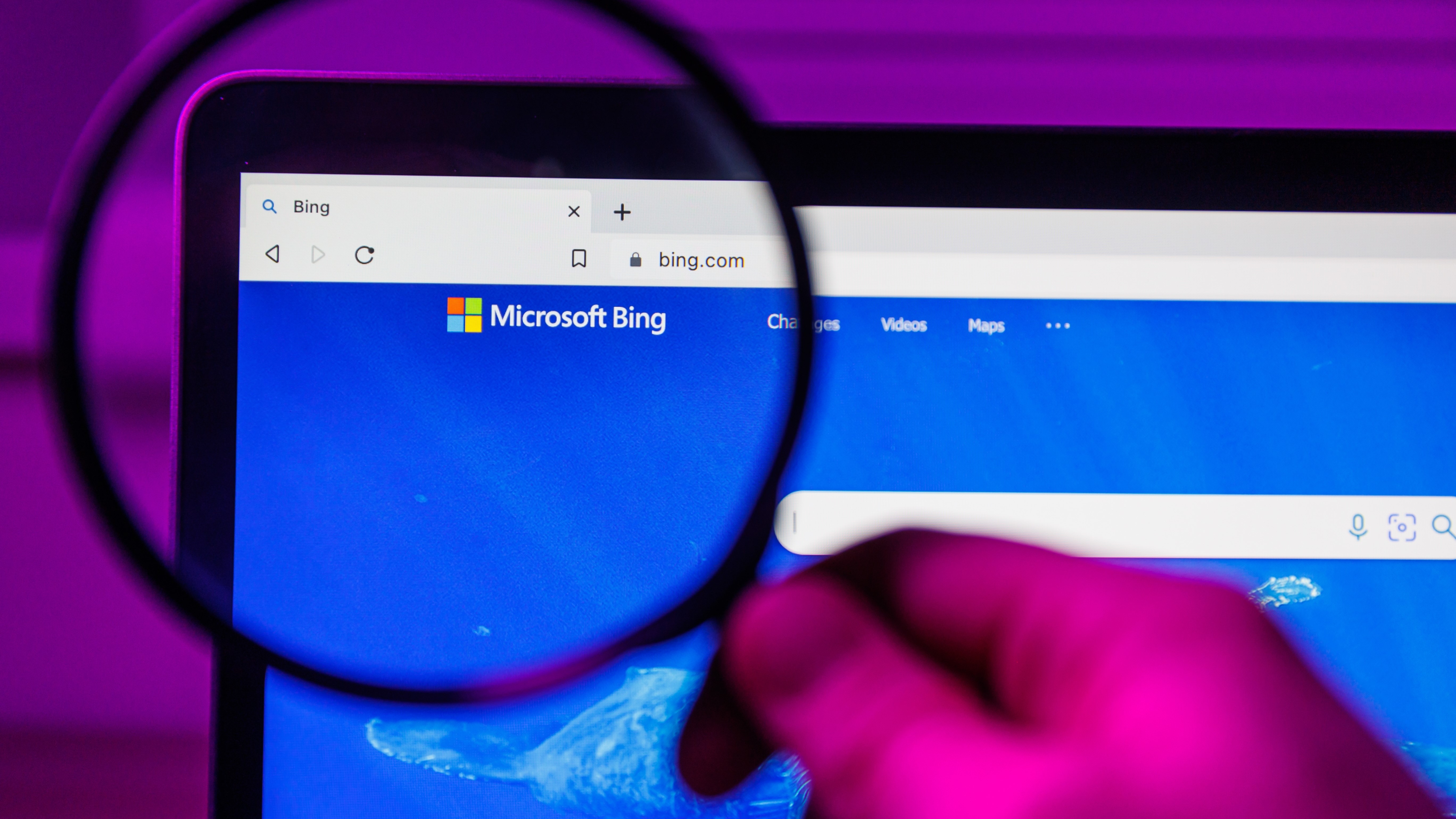 Microsoft's Bing logo magnified through a magnifying glass, looking at a screen