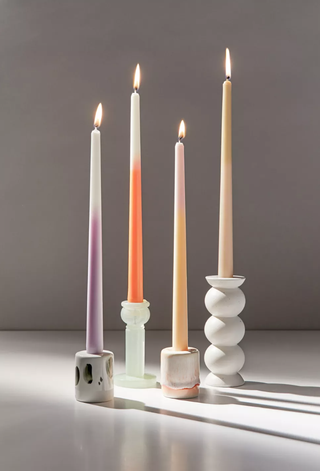 four ombre candles of different colors sit in stoneware holders of varying height