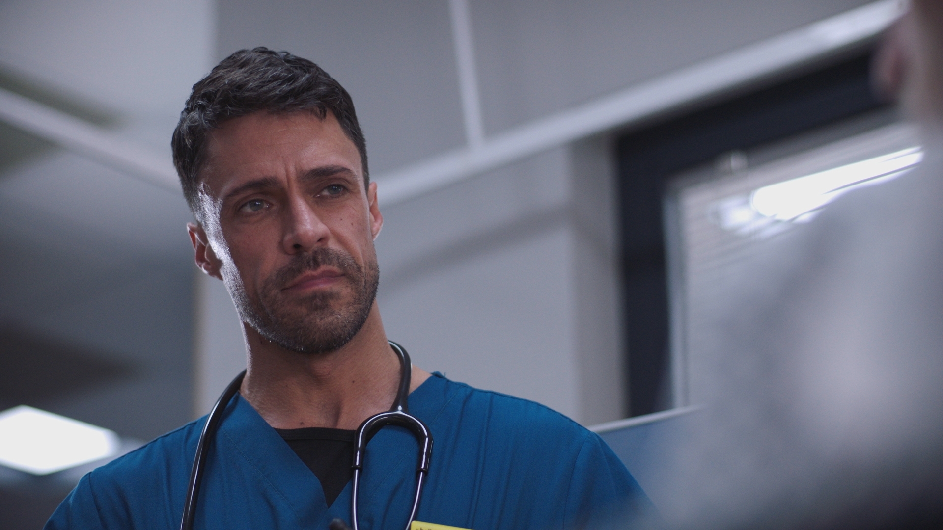Flynn Byron in his blue hospital scrubs looking disdainful.