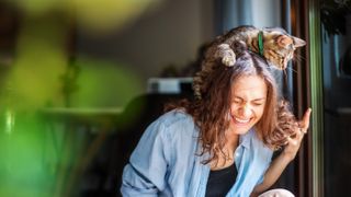 Woman laughing happily with a cat on her head