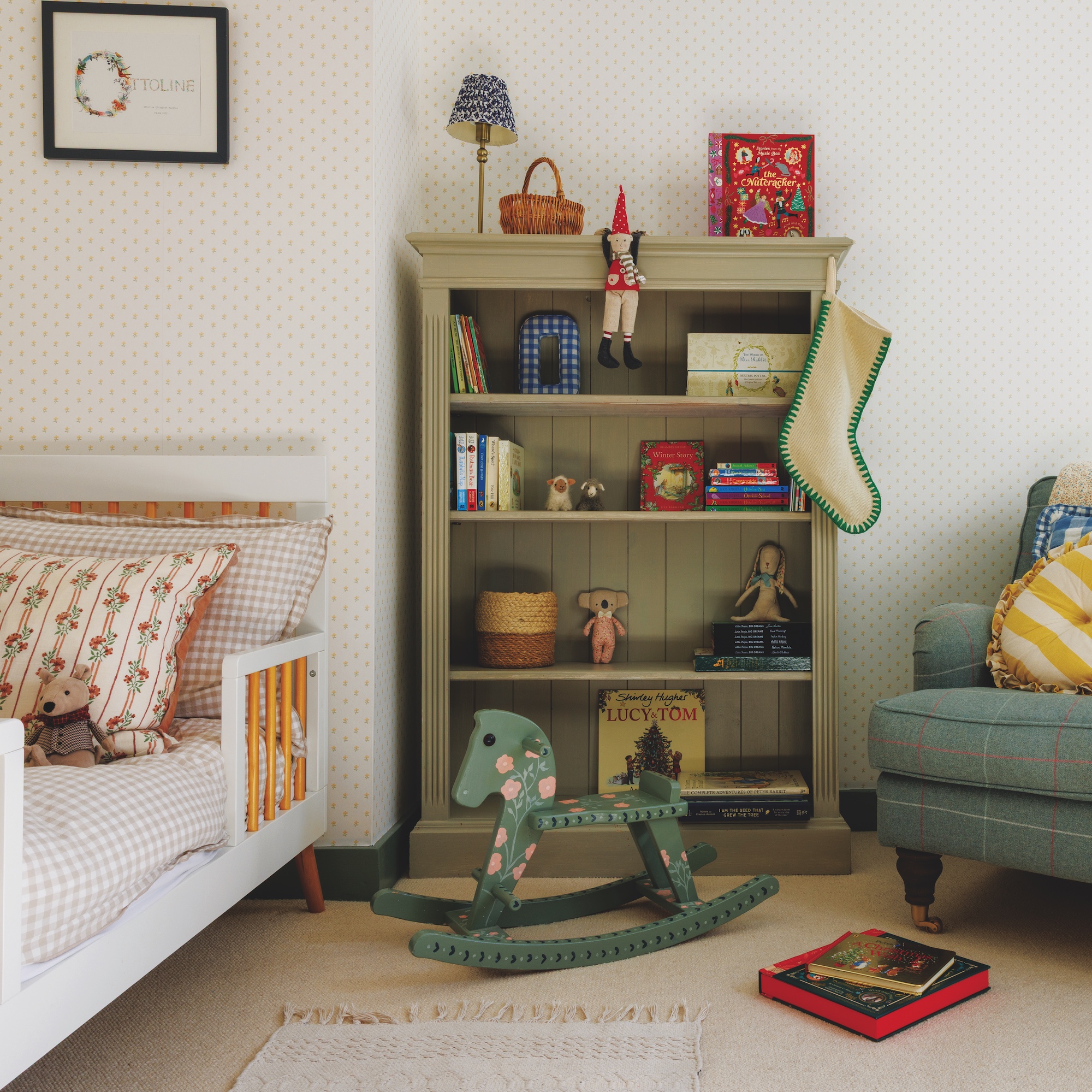 girl&#039;s bedroom with low white bed with gingham bedding, green painted bookcase and blue tweed armchair