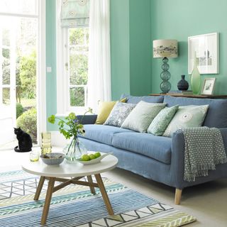 living room with with blue wall blue sofa with designed cushion and white windows