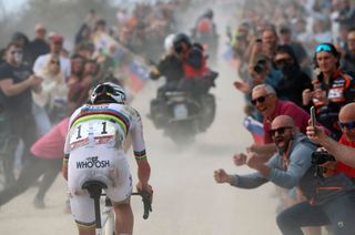 Tadej Pogacar rides up a gravel climb with the crowd cheering him on, his kit torn and bloodied from a crash