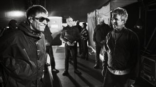 Liam Gallagher and Noel Gallagher share a rare, smiling moment backstage in a grainy black-and-white photo while surrounded by their crew.