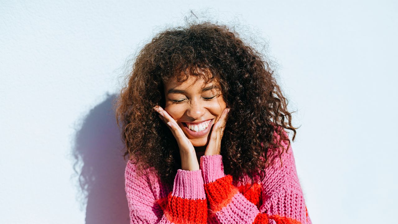 Portrait of laughing young woman with curly hair against white wall - stock photo