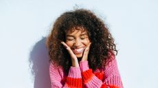 Portrait of laughing young woman with curly hair against white wall - stock photo