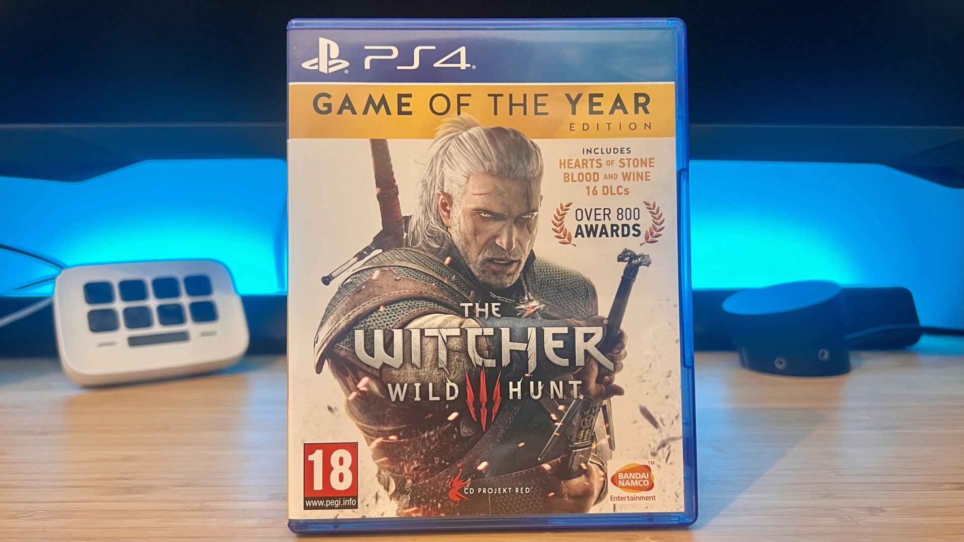 A PS4 copy of The Witcher 3 Wild Hunt on a wooden desk with blue backlighting