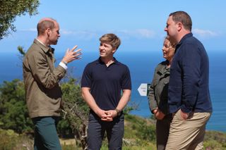 Prince William talking to Robert Irwin, a man and woman in front of the ocean